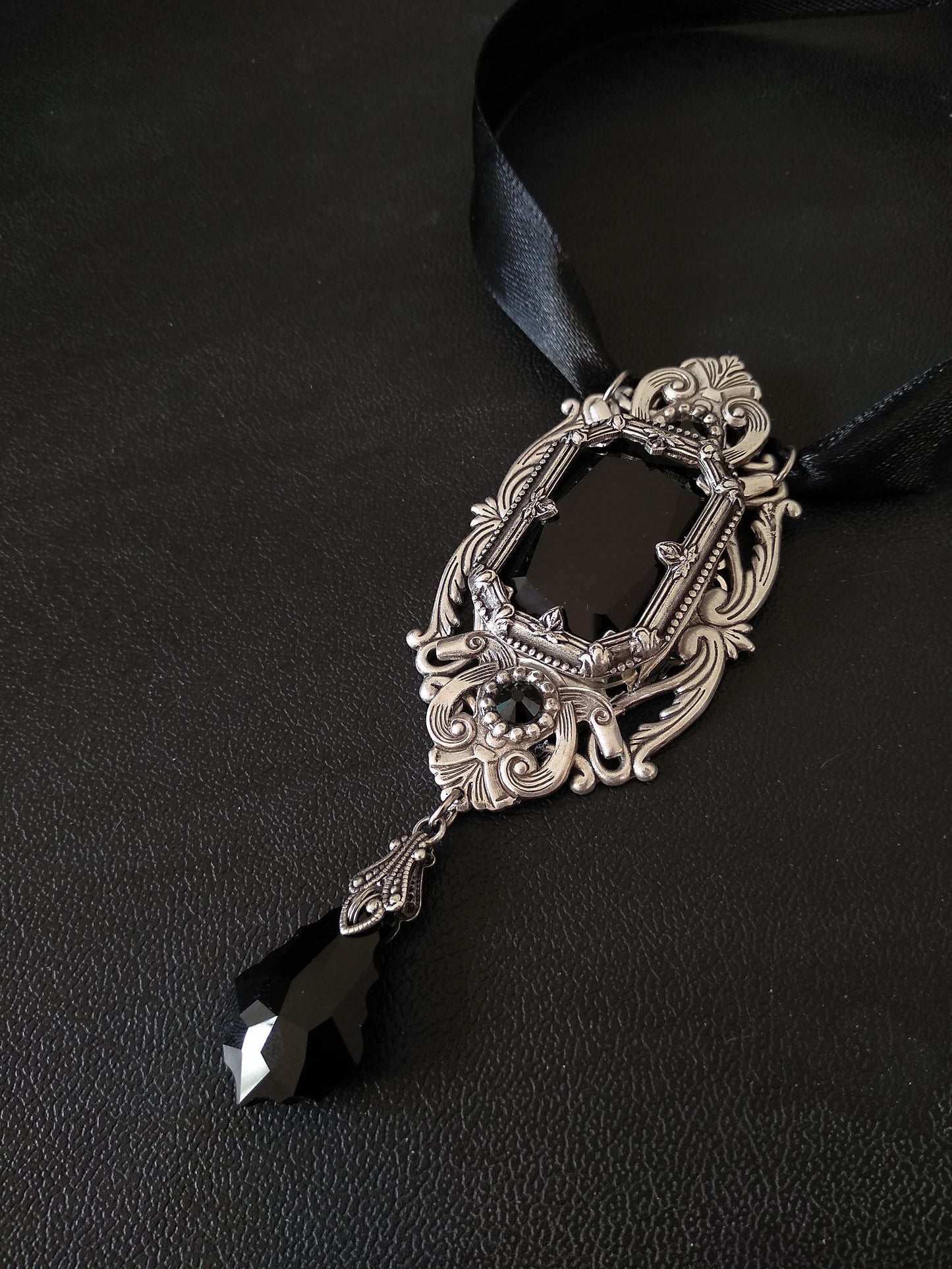 Elegant black and silver necklace featuring a silver pendant and a satin ribbon adorned with a black crystal stone.