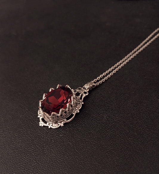 Ornate necklace showcasing a beautiful dark red gem in intricate silver setting.
