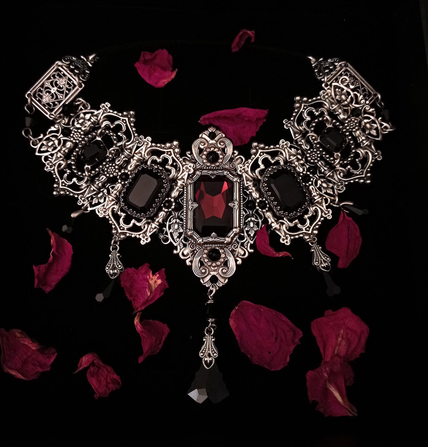 Most grand riviere gothic choker with intricate silver accents, a focal Burgundy stone and smaller black ones.
