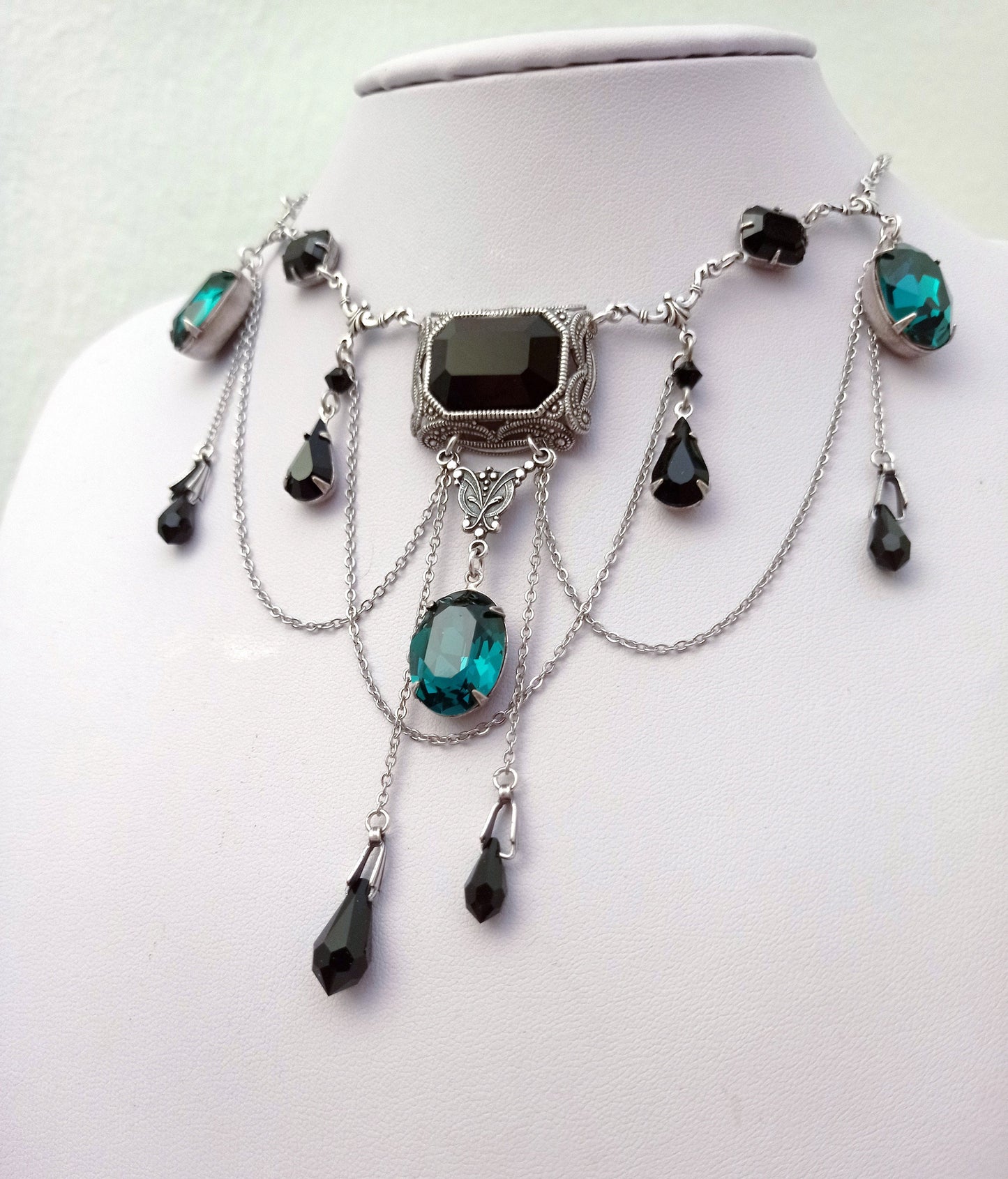 Gothic necklace with black and green Swarovski crystals, silver filigree centerpiece, and draping chains on display bust. Elegant vampire style jewelry. Gothic jewelry.
