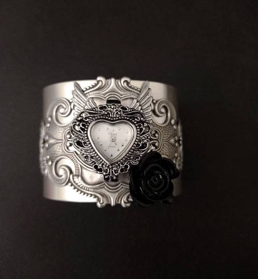 Wide silver cuff bracelet with flourishes, wings, a black rose and a heart shaped watch face.