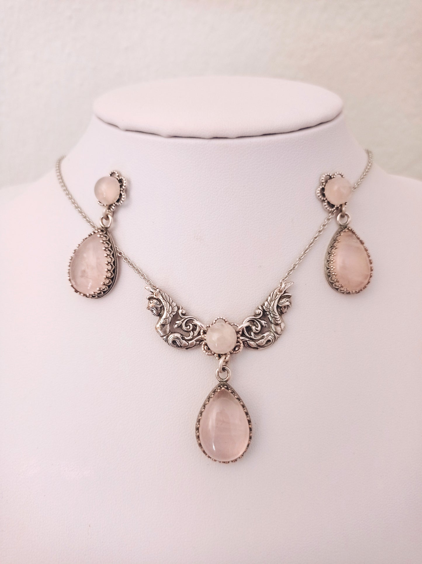 Rose Quartz necklace and earrings set featuring ornate detailing and matching pink teardrop-shaped stones. The set includes drop earrings and a necklace with three stones in decorative frames.