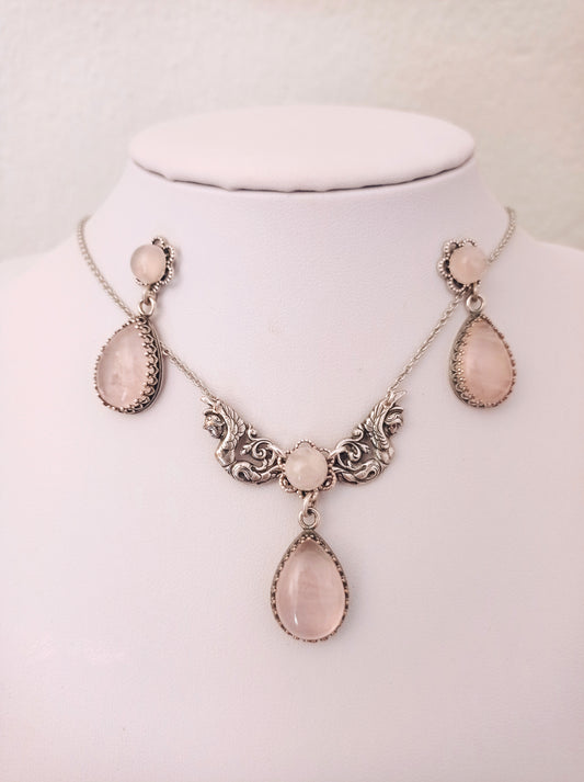 Rose Quartz necklace and earrings set featuring ornate detailing and matching pink teardrop-shaped stones. The set includes drop earrings and a necklace with three stones in decorative frames.