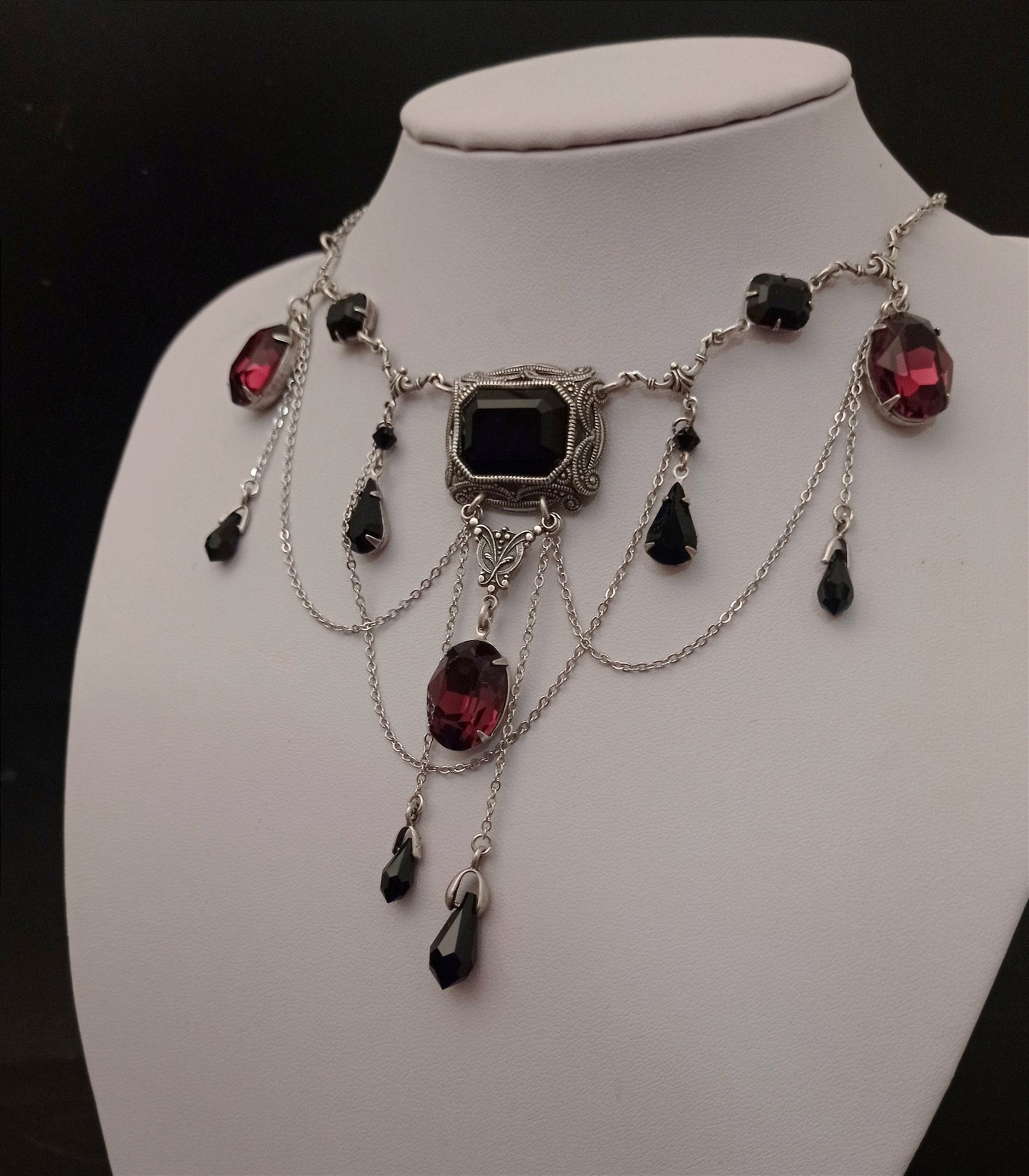 Bold silver necklace with black and burgundy gemstones, featuring intricate cascading chain and a large central black stone in an ornate setting.