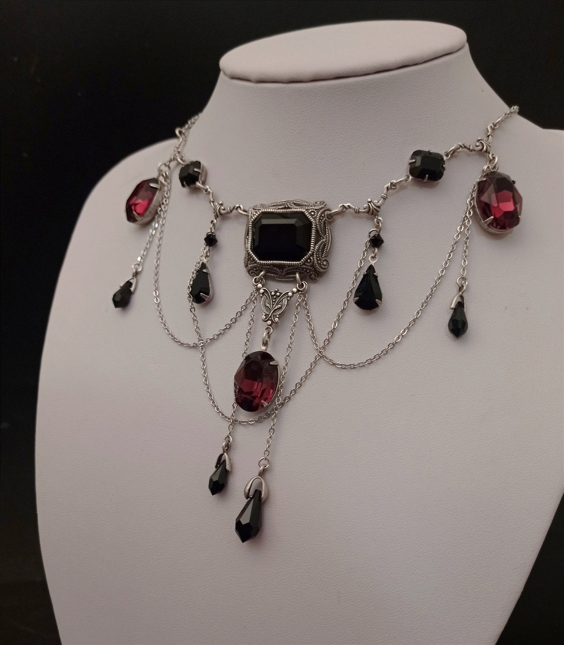 Bold silver necklace with black and burgundy gemstones, featuring intricate cascading chain and a large central black stone in an ornate setting.