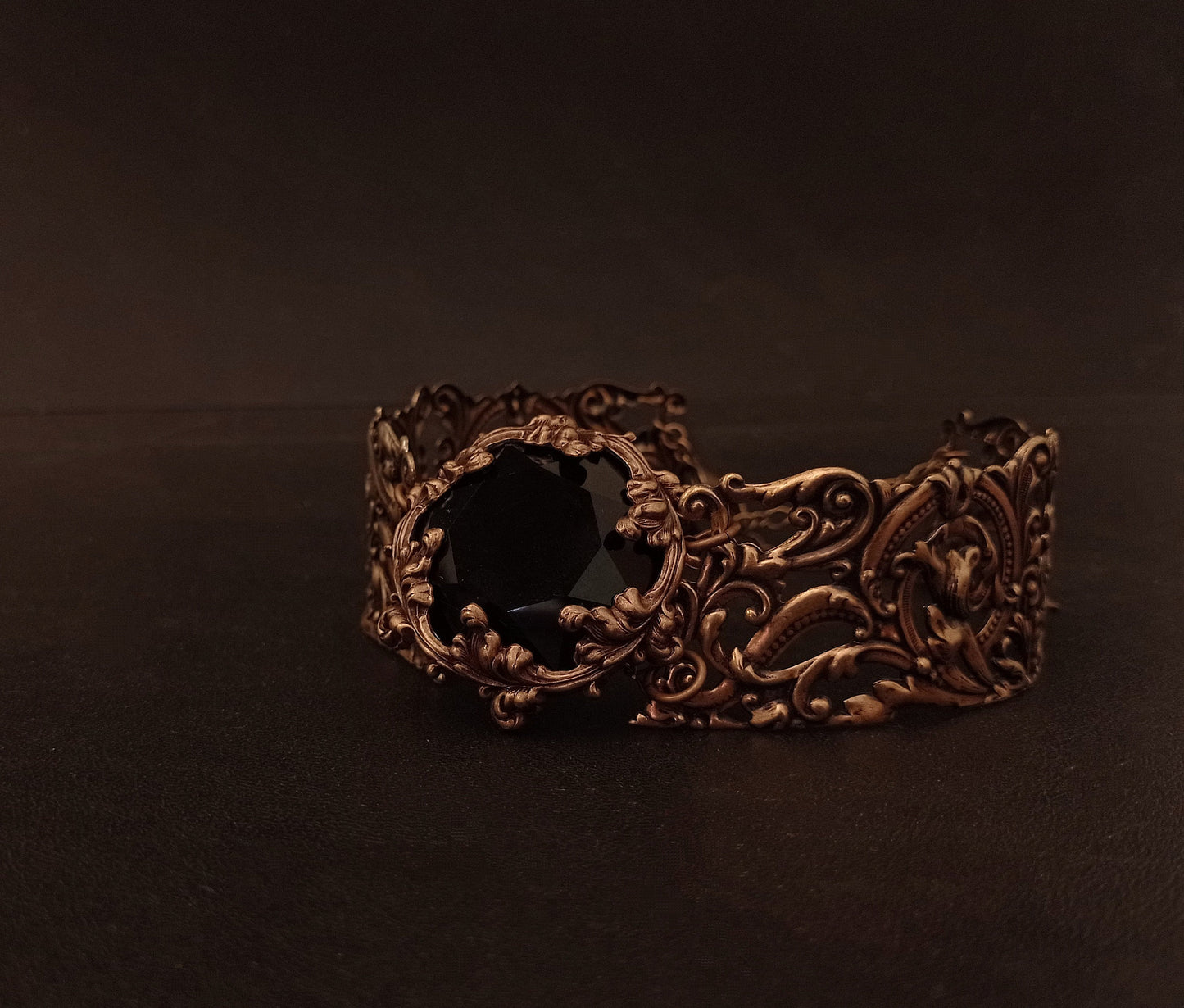 Intricately detailed wide brass choky featuring a large black gemstone at its center, resting on a dark textured surface.
