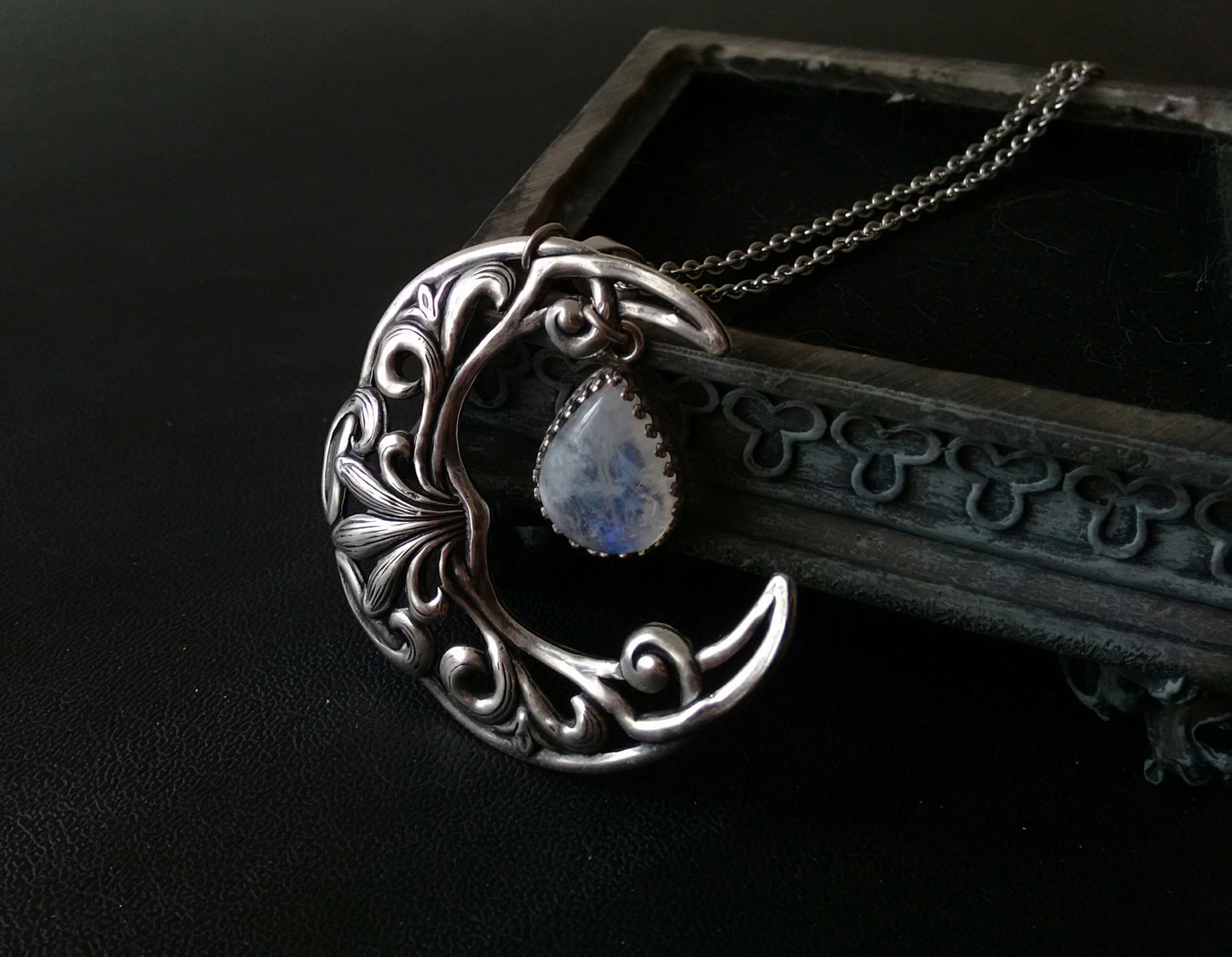 A silver plated necklace featuring a crescent moon pendant with intricate celtic patterns and a rainbow moonstone cabochon in the center.