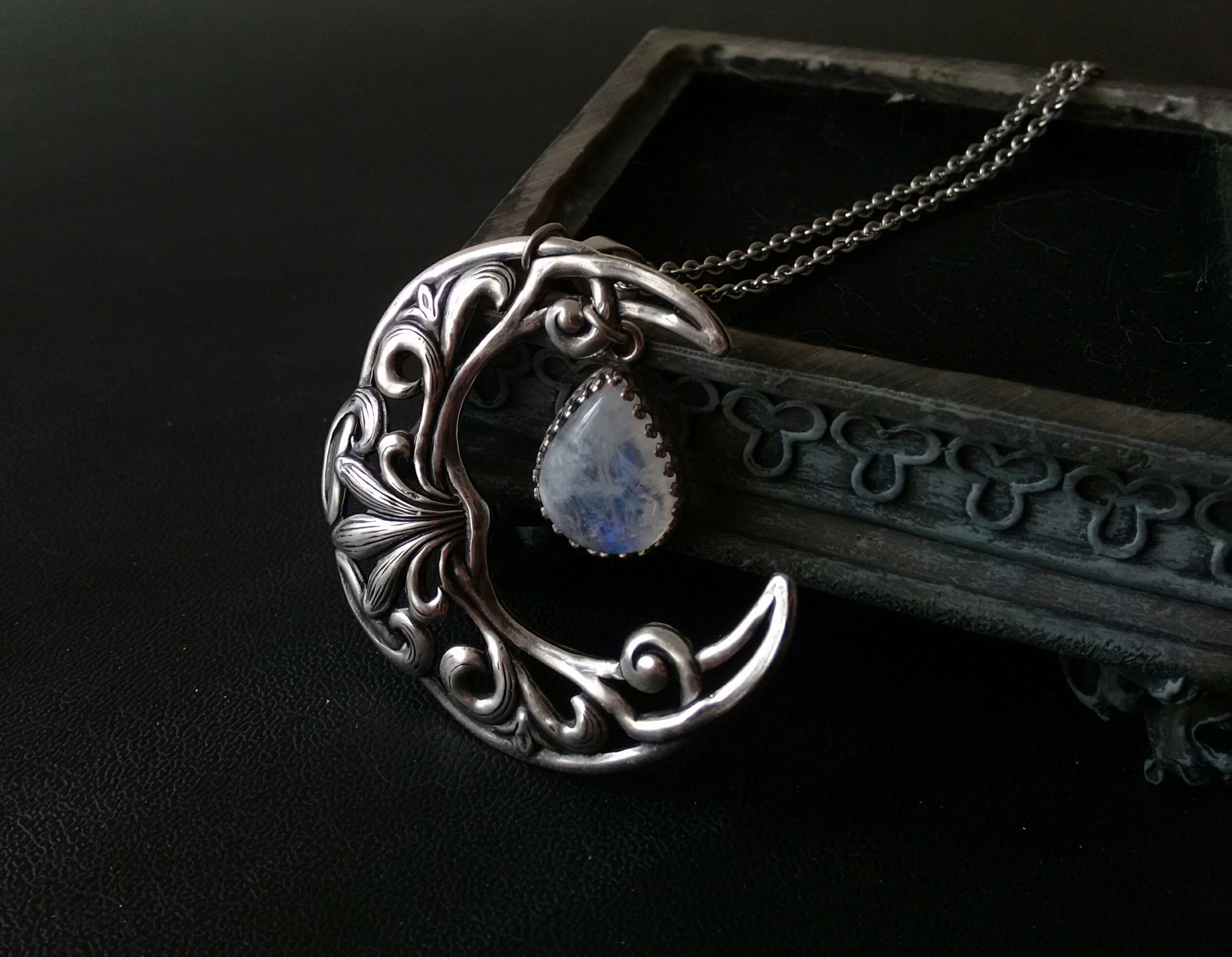 A silver plated necklace featuring a crescent moon pendant with intricate celtic patterns and a rainbow moonstone cabochon in the center.
