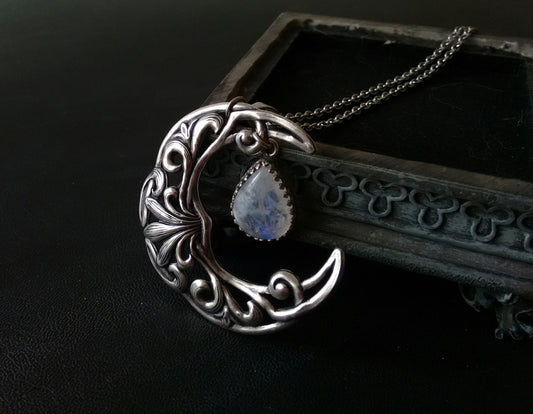 A silver plated necklace featuring a crescent moon pendant with intricate celtic patterns and a rainbow moonstone cabochon in the center.