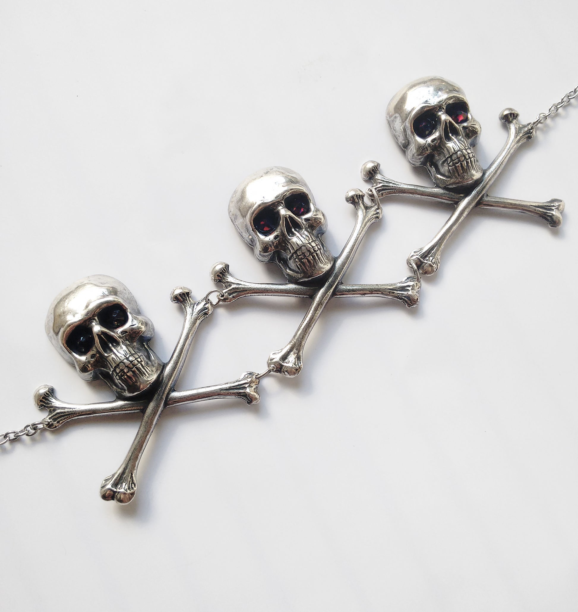 Add macabre flair to your look with this Large silver skulls and crossbones Gothic choker, with burgundy crystals set in their eyes! Nickel and lead free.