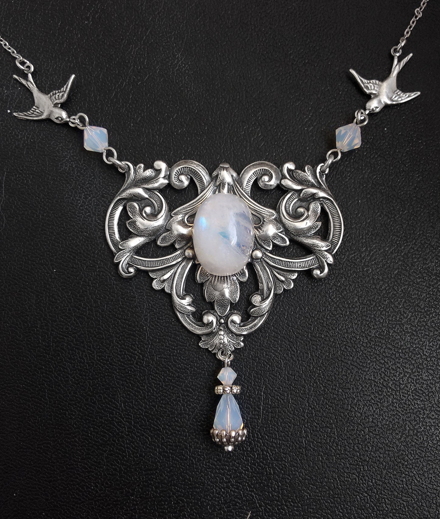 A Victorian style necklace with floral motifs, two birds in flight, and a rainbow moonstone pendant, adorned with swarovski crystals in white/blue colors.