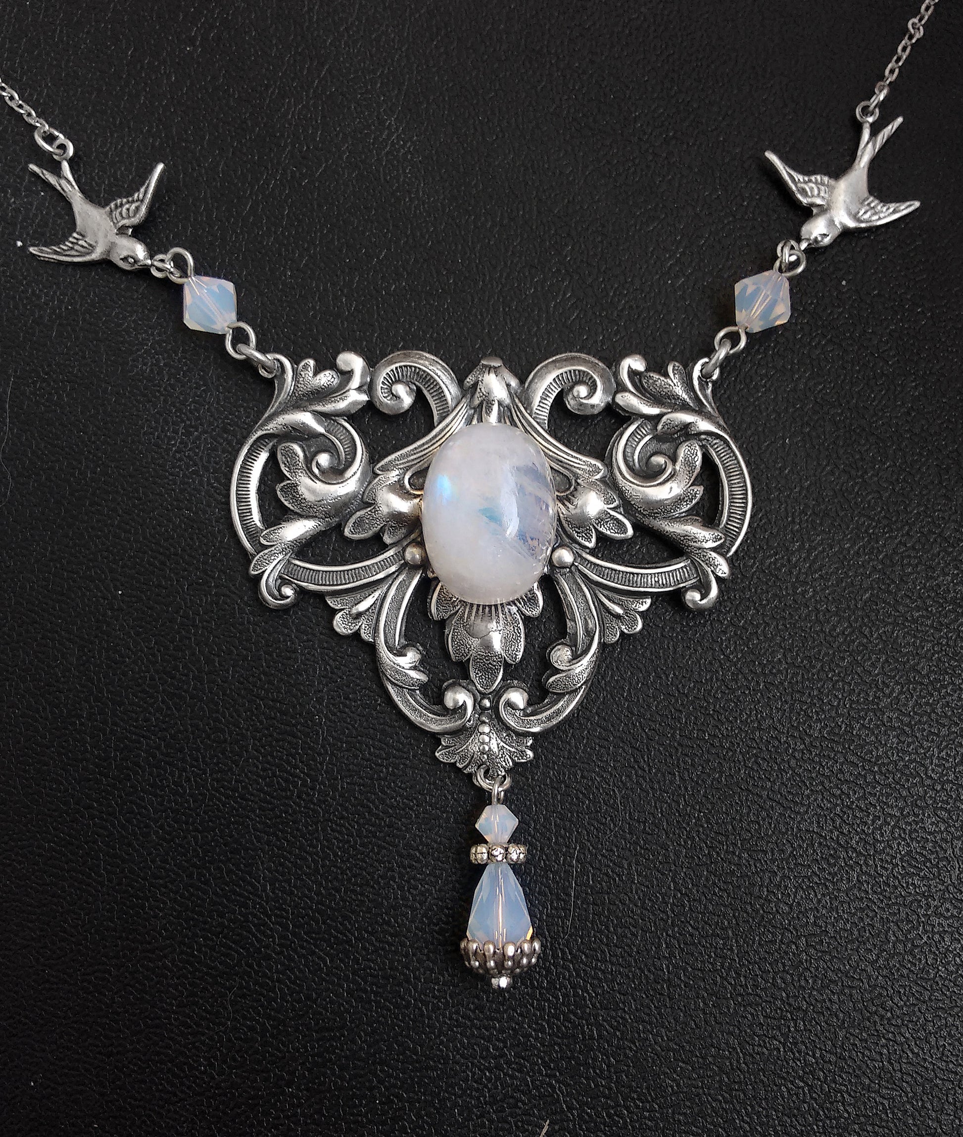 A Victorian style necklace with floral motifs, two birds in flight, and a rainbow moonstone pendant, adorned with swarovski crystals in white/blue colors.