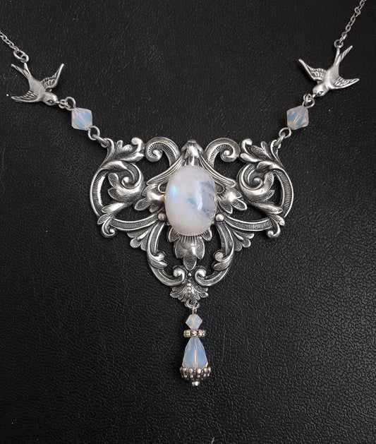 A Victorian style necklace with floral motifs, two birds in flight, and a rainbow moonstone pendant, adorned with swarovski crystals in white/blue colors.